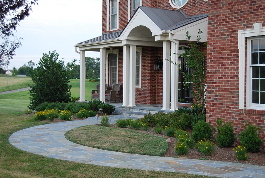 A stone pavers walkway with grass on either side leading to the front door of a brick house