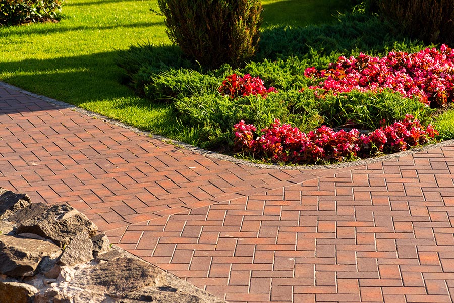 A brick path walkway in the front of a house, running between a garden and a rock display