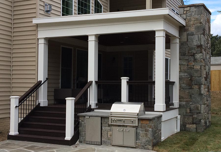 A porch with dark brown wooden plank flooring and white pillars.