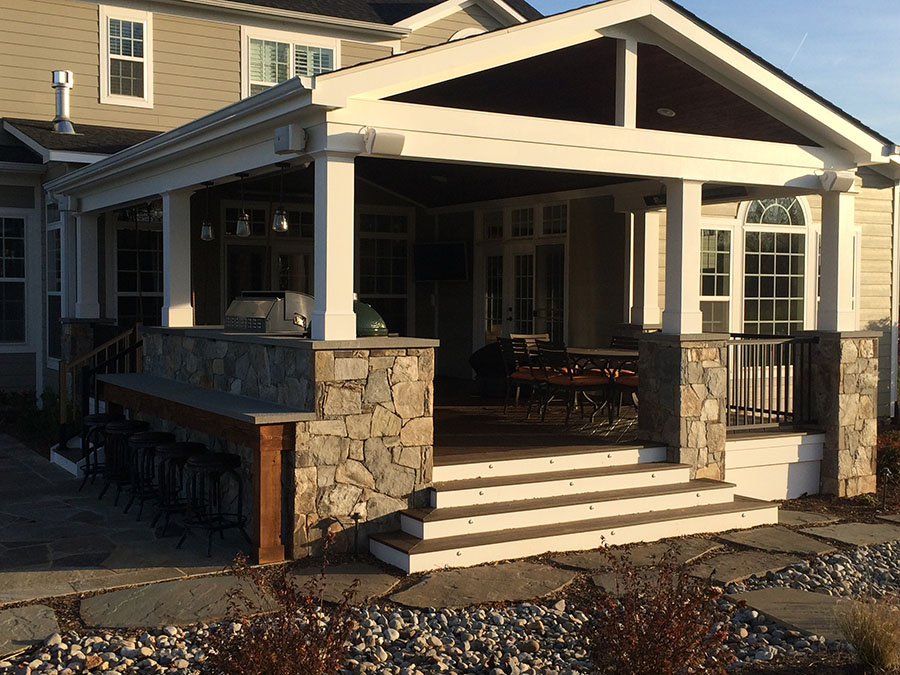 A covered porch with a grill. A table and chairs sit near the stairs.