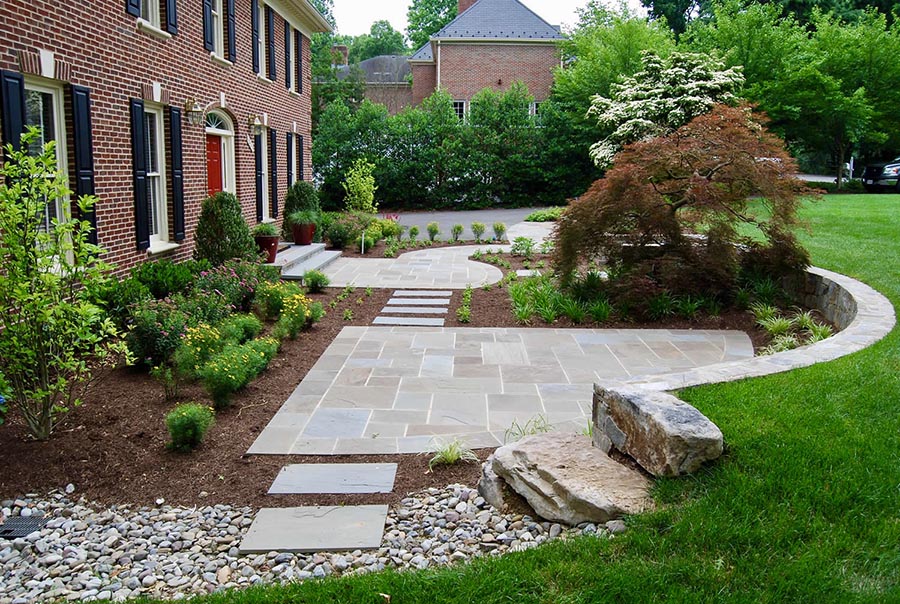 A stone walkway leading to a brick house’s back door