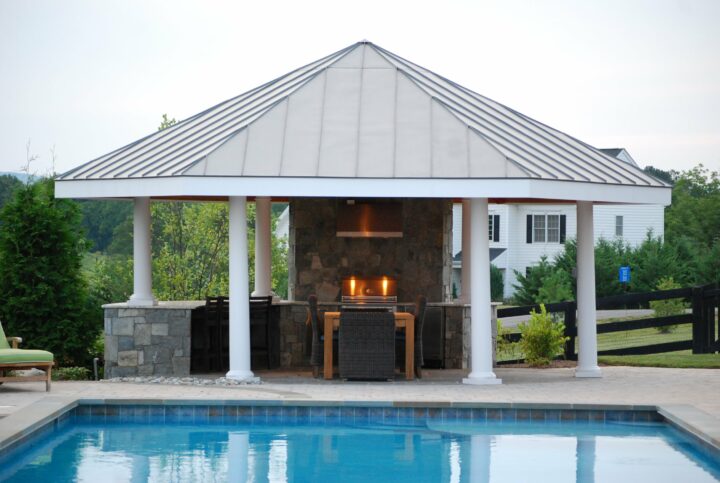 An outdoor kitchen next to a pool with a white pavilion on top