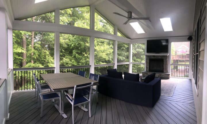 A screened-in porch with a television & fireplace, couch, and dining table