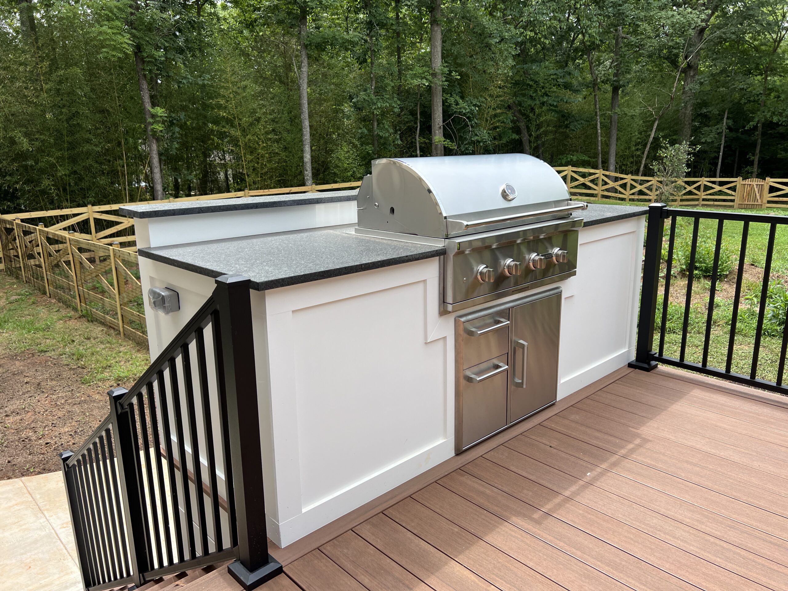 An outdoor kitchen with a grill and countertop space up against the edge of a wood deck