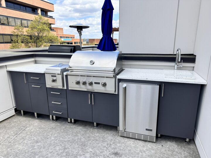 An outdoor kitchen up against a balcony with marble countertops and gray cabinetry.
