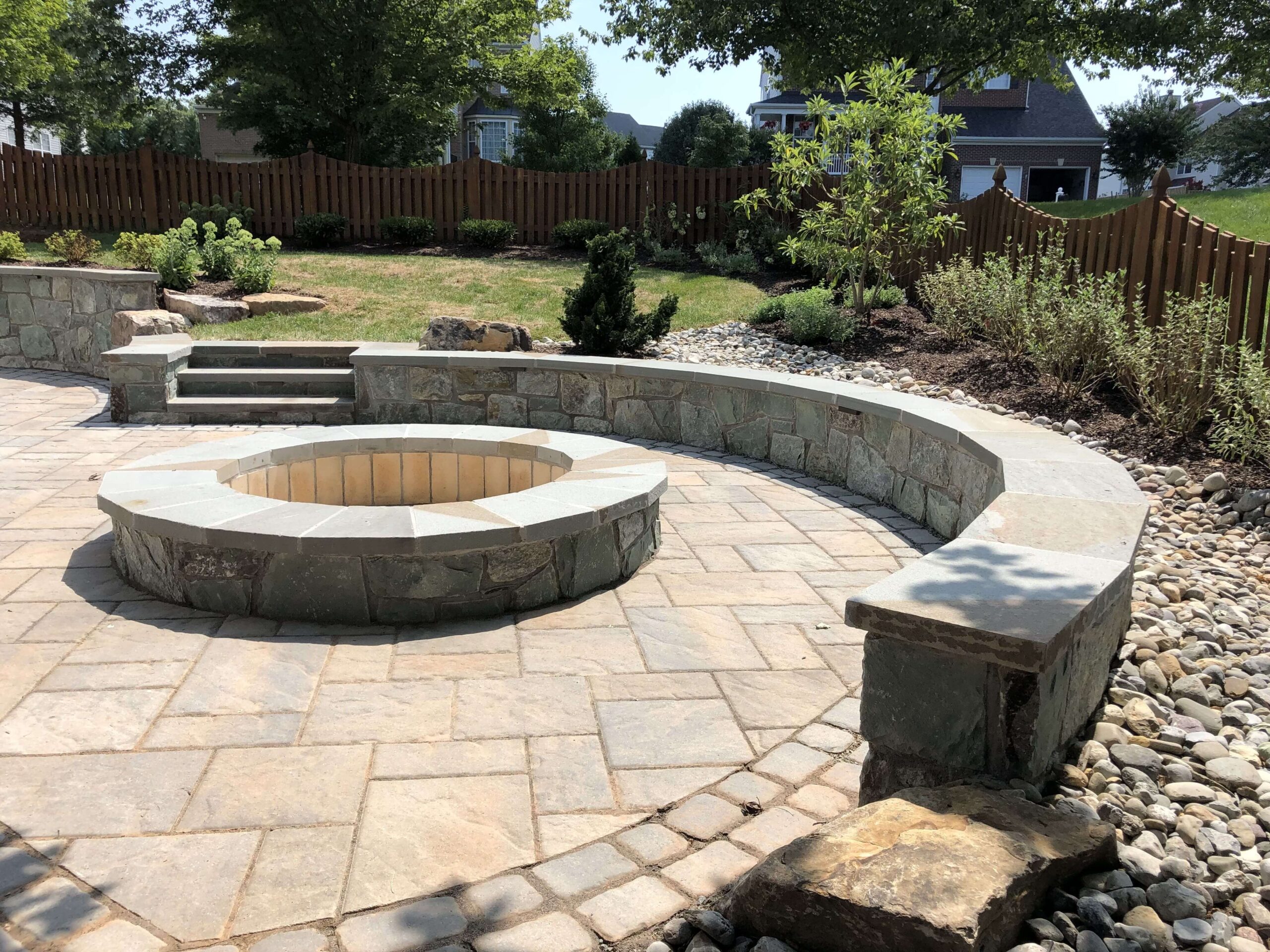 A circular stone pavers patio with a circular fire pit in the center and a retaining wall on the edge.