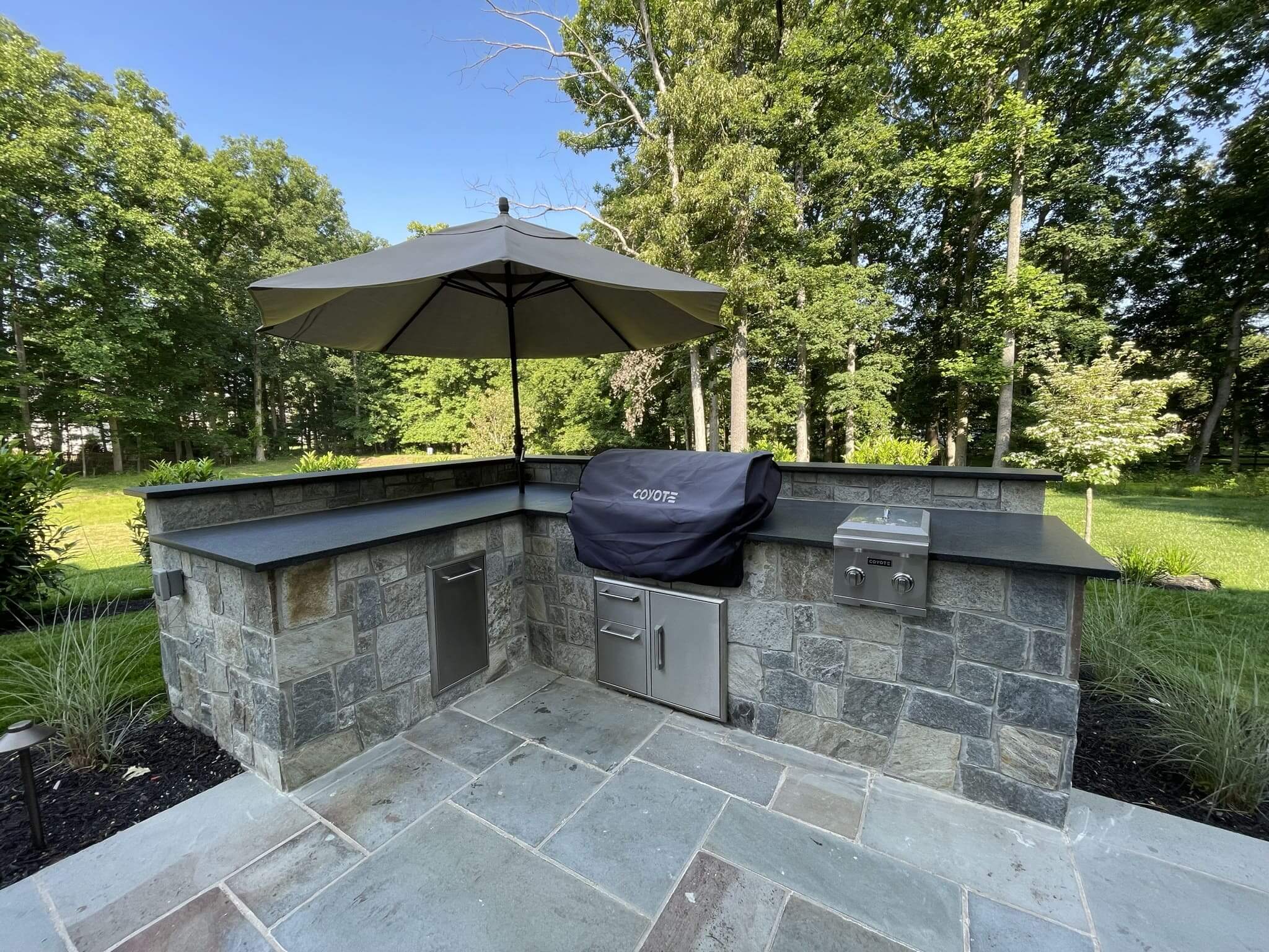 A pavers patio with an outdoor kitchen sitting on the corner of the patio.