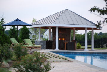 A poolside pavilion with an outdoor kitchen and fireplace.