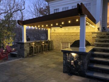 An attached pergola with bar seating and bistro lighting.