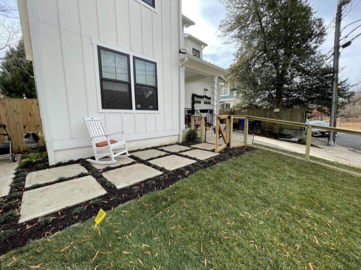 A series of eight large square stepping stones placed in the dirt outside of a home.